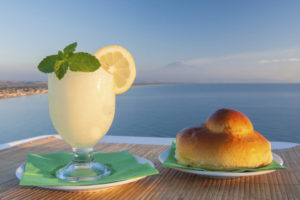 Sicilian lemon granita and a typical warm brioche with blue sea and Mount etna in the background